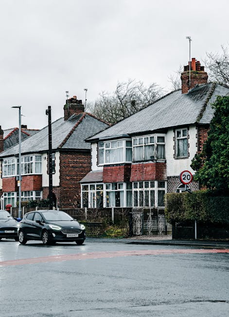An exterior view of a row of terraced houses on Honor Oak Road, each painted in different pastel colors, including blue, pink, beige, and pale green. The houses feature white window frames and decorat